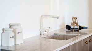 Una cucina con un piano di lavoro in marmo bianco, un rubinetto moderno e due barattoli etichettati 'SUCRE' e 'BISCUIT'.