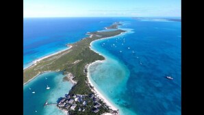 Vista aérea de un balneario costero con una extensa playa, aguas azules cristalinas y varias embarcaciones.