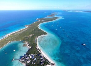 An aerial view of a coastal resort with a long stretch of beach, clear blue waters, and several boats.