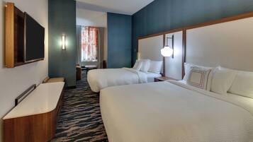 Habitación de hotel con una cama grande, una cama más pequeña, un escritorio con silla, un televisor de pantalla plana en la pared y un baño con bañera.