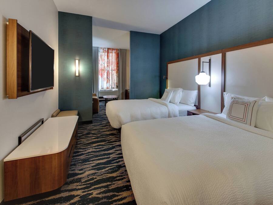 Habitación de hotel con una cama grande, una cama más pequeña, un escritorio con silla, un televisor de pantalla plana en la pared y un baño con bañera.