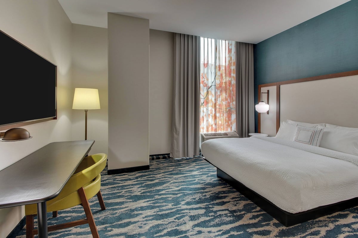 A hotel room with a bed, a desk, a chair, a lamp, and a window with curtains.