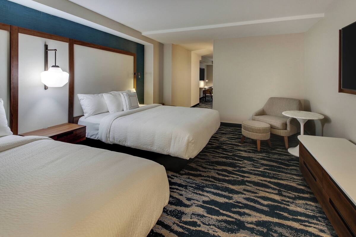 A hotel room with two beds, a small desk, a chair, and a round table.