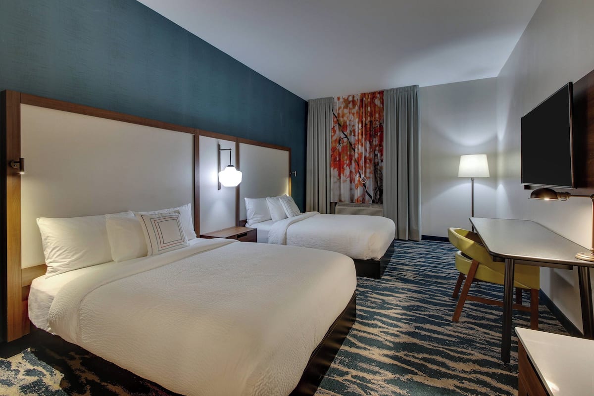 A hotel room with two beds, a desk, and a chair.