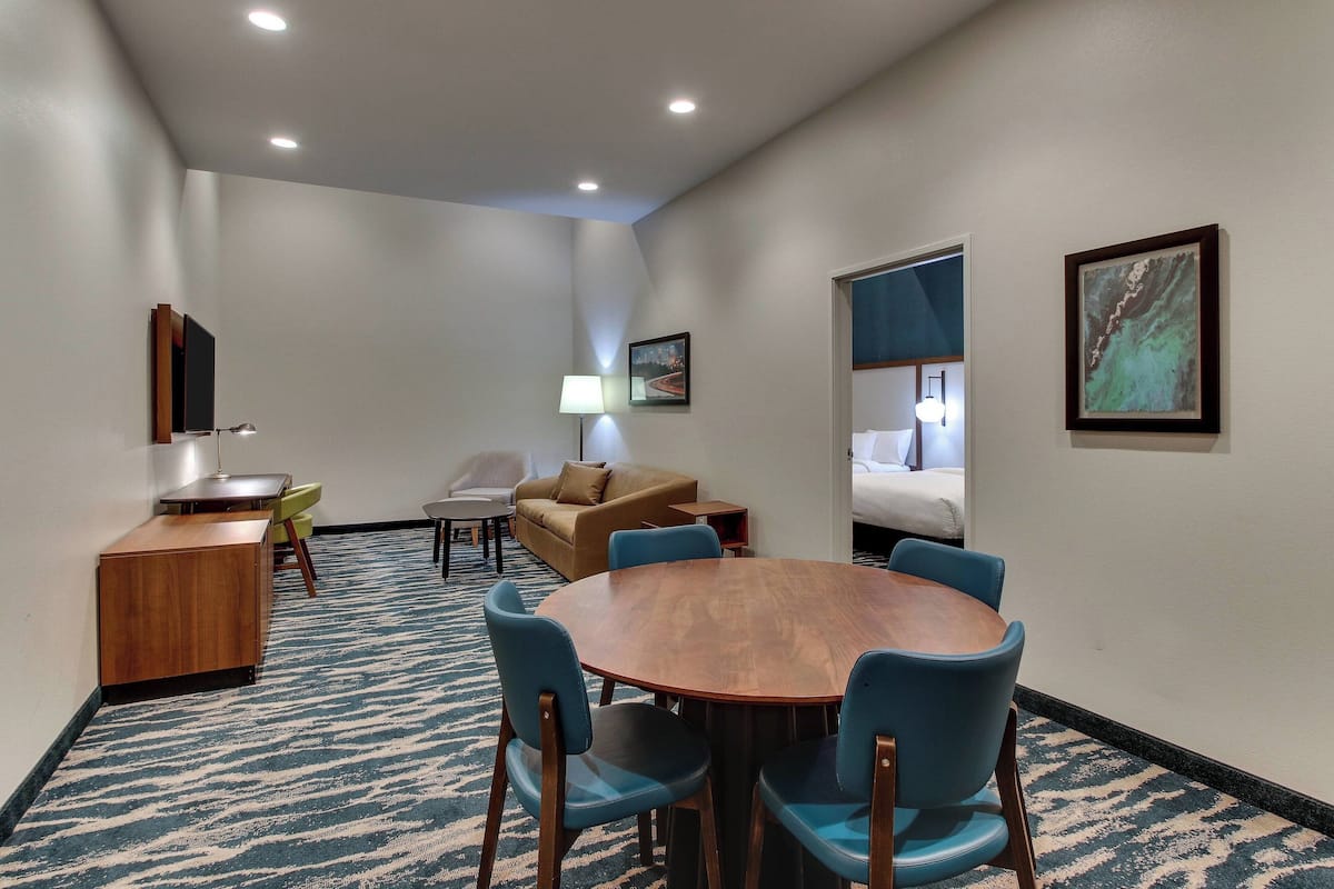A hotel room with a round wooden table, blue chairs, a sofa, a desk, and a lamp.