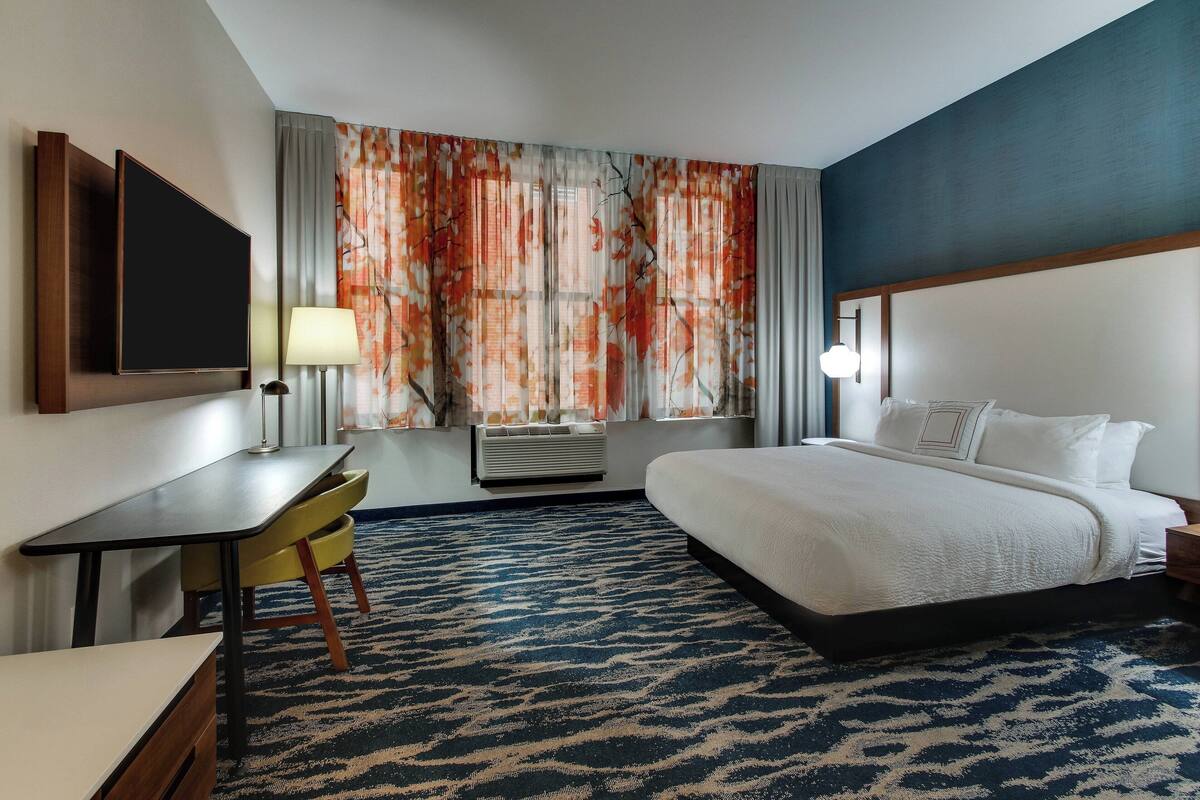 A hotel room with a bed, a desk, a chair, a TV, and a window with curtains.