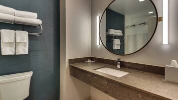 A modern bathroom with a marble sink, a large mirror, and a towel rack with folded towels.