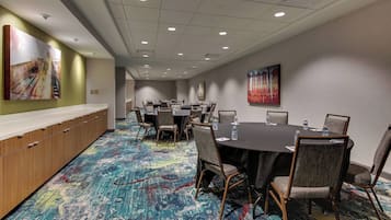 A conference room with a long table and chairs, a wooden cabinet, and a colorful carpet.