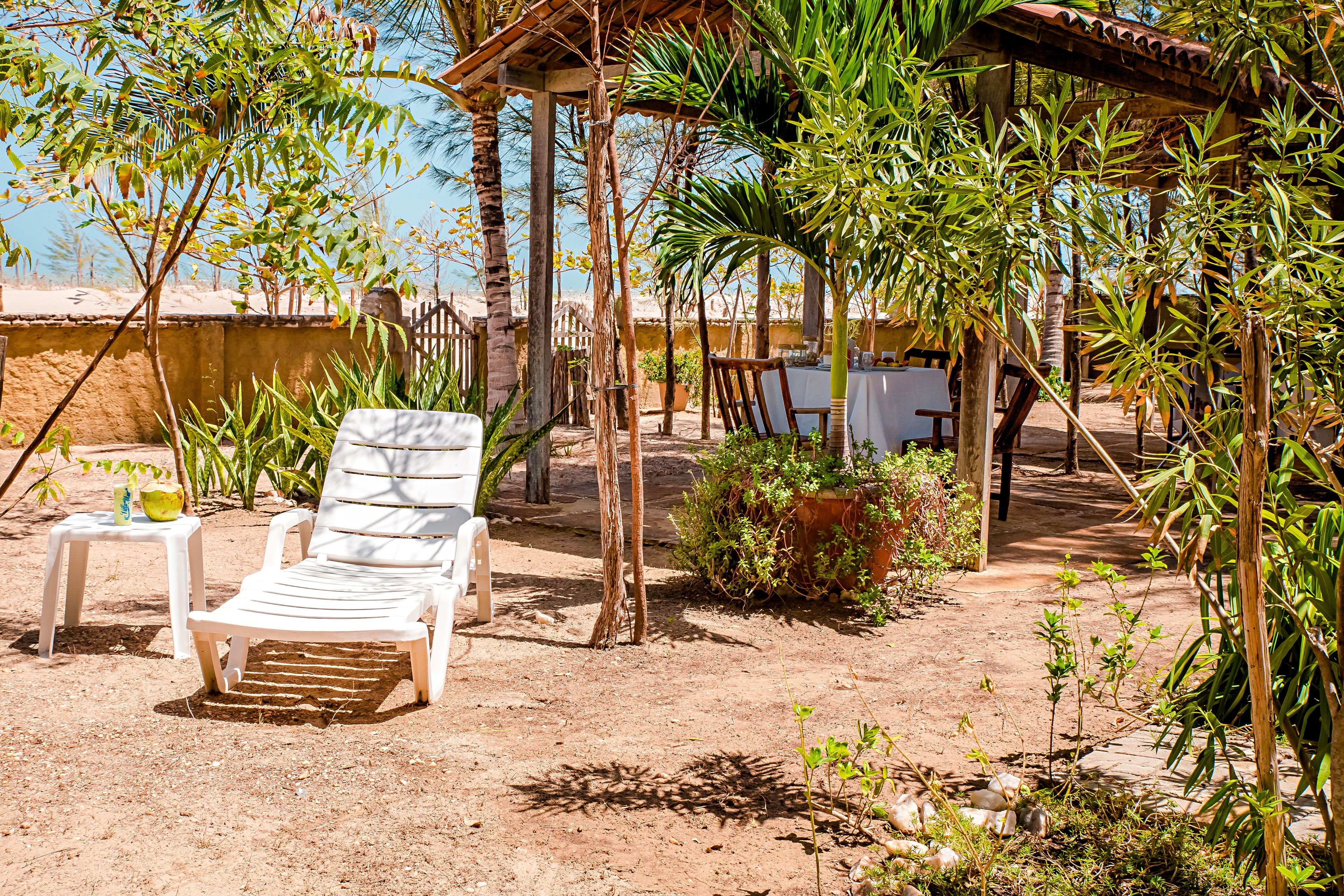 A covered outdoor seating area with a white lounge chair, a small table with a drink, and a potted plant.