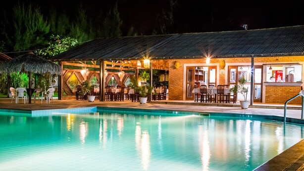A poolside area with a covered seating area, a pool, and a building with a brick facade. - Villa del Mar Praia hotel - Frente a Praia (Camocim)