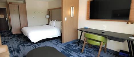 A hotel room with a bed, desk, chair, and a flat-screen TV.