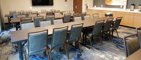 A conference room with a long table, multiple chairs, a television, a coffee station, and a door.