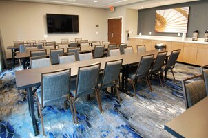 Un salón de conferencias con una mesa larga, varias sillas, un televisor, una estación de café y una puerta.