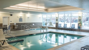 An indoor swimming pool with clear glass walls, a tiled floor, and a few chairs around the pool area.