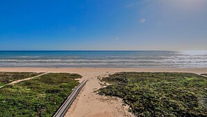 Une plage avec une promenade dallée qui mène à l’eau, entourée de verdure.