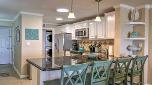 Une cuisine avec des meubles blancs, un plan de travail en granit et des chaises de couleur turquoise.
