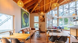 A spacious dining area with wooden tables and chairs, large windows offering views of the outdoors, and various artworks on the walls.