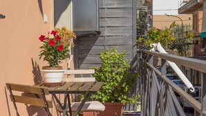 A balcony with a wooden table and chairs, potted plants, and a railing. - Casa Amica Giardini Naxos (Giardini Naxos)
