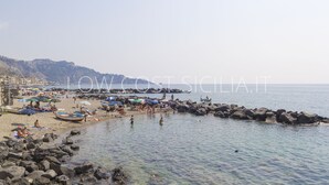 A beach with rocky shorelines, clear water, and people enjoying the sun. - Casa Amica Giardini Naxos (Giardini Naxos)