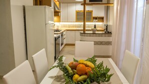 A modern kitchen with white cabinets, a dining table with chairs, and a fruit bowl on the table. - Casa Amica Giardini Naxos (Giardini Naxos)