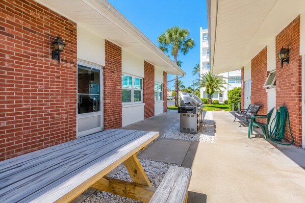 A covered outdoor patio with a barbecue grill, seating area, and a hose for cleaning.