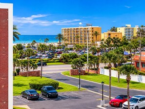 A hotel with a parking lot, palm trees, and a view of the ocean.