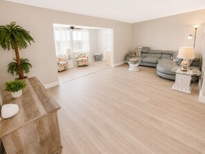 A spacious living room with a grey sofa, a coffee table, and a plant.