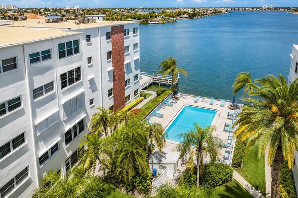 A modern building with a swimming pool, palm trees, and a view of the water.