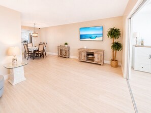 A spacious living area with a dining table, chairs, a TV, and a large window.