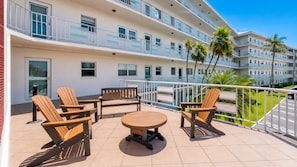 Un balcón con mobiliario exterior, una piscina y vistas a palmeras y una carretera.