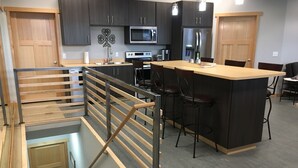 Een moderne keuken met donkere kastjes, roestvrijstalen apparatuur, een centraal eiland met barkrukken en een glazen ruimte beneden.