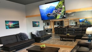 Een moderne woonkamer met een grote flatscreen-tv, een bank, een salontafel met appels en een keuken op de achtergrond.