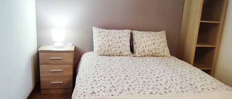 A bedroom with a bed, a nightstand with a lamp, and a wooden wardrobe.