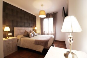 A hotel room with a bed, two bedside lamps, a TV, and a window with curtains. - 1093 Villa Magnolias (Torrox)