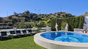 Une piscine dont le bord est recouvert de carreaux, entourée de gazon synthétique, et ornée de deux statues blanches.