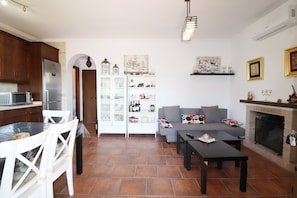 A modern living room with a sofa, coffee table, and fireplace. There is a dining area with chairs and a table. The room has a tiled floor and white walls. - 1093 Villa Magnolias (Torrox)