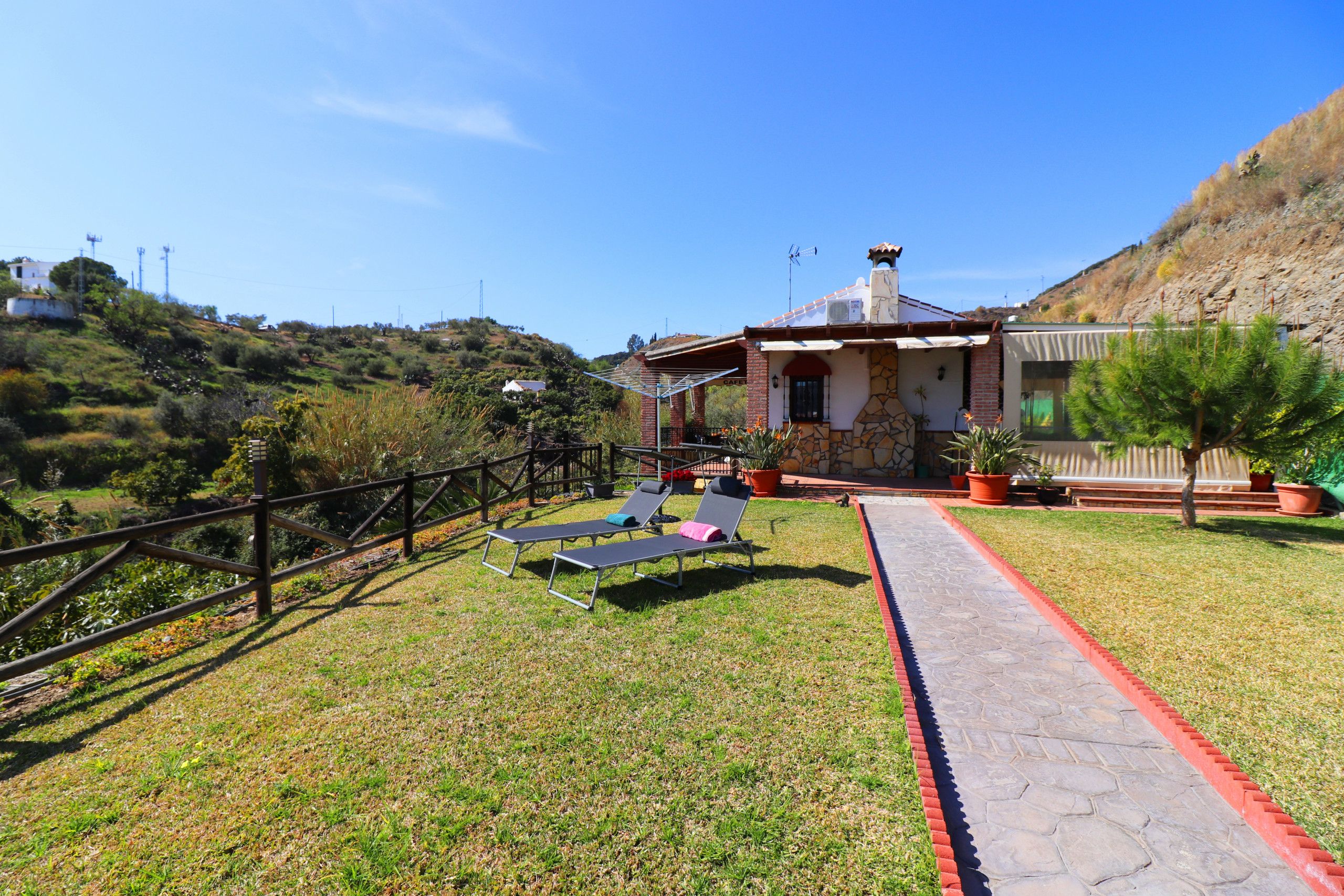 A house with a stone facade, a red pathway, and two lounge chairs with cushions.