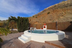 A circular hot tub with steps leading into it, surrounded by a wooden deck and a stone wall. - 1093 Villa Magnolias (Torrox)