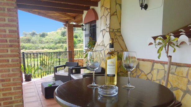 Une terrasse avec une table ronde, deux chaises, une bouteille de vin et deux verres à vin.