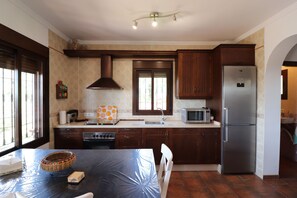 A kitchen with wooden cabinets, a stainless steel refrigerator, a microwave, and a stove. - 1093 Villa Magnolias (Torrox)
