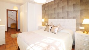 Une chambre à coucher avec un grand lit, deux tables de chevet avec des lampes, une armoire et une porte donnant sur un escalier.