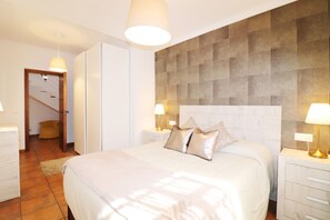 A bedroom with a large bed, two bedside tables with lamps, a wardrobe, and a door leading to a staircase. - 1093 Villa Magnolias (Torrox)