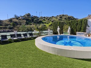 A swimming pool with a tiled edge, surrounded by artificial grass, and two white statues. - 1093 Villa Magnolias (Torrox)
