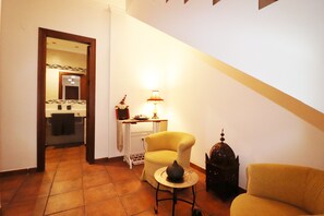 Un salon avec un fauteuil jaune, une petite table ronde ornée d’un objet décoratif, une lampe et un meuble de couleur sombre.