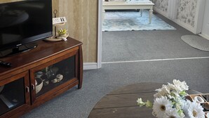 A living room with a television on a wooden stand, a coffee table with a welcome sign, and a floral arrangement.