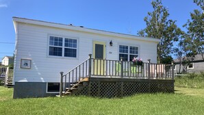 A white mobile home with a small porch and a green door, number 232, surrounded by grass.