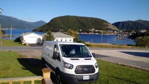 A white van parked on a road with a lake and mountains in the background.