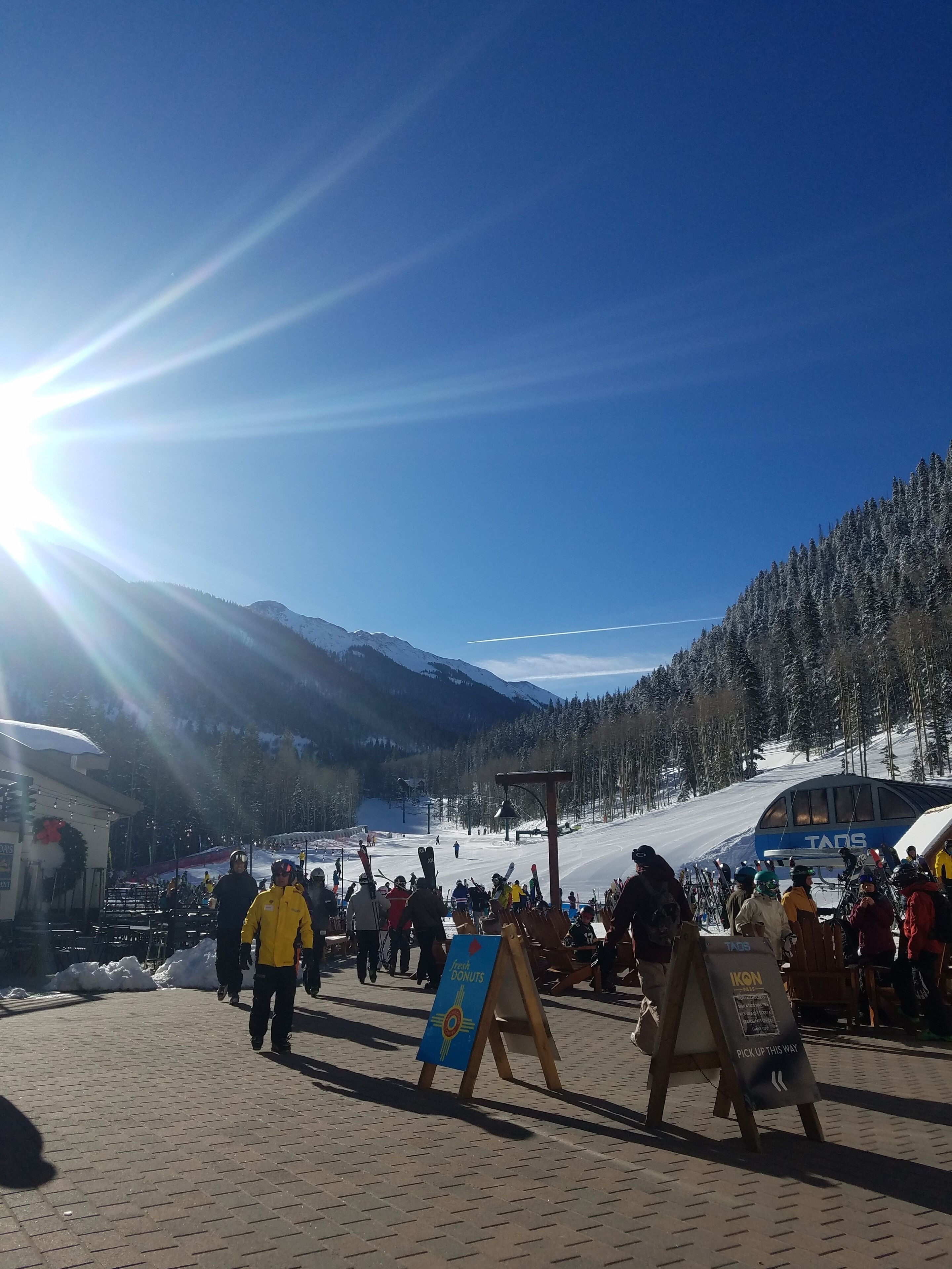 A ski resort with a clear sky, a sun shining, and people walking.