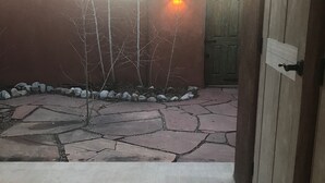 Un chemin pavé mène à une porte en bois, avec un mur de pierre et un petit arbre en arrière-plan.