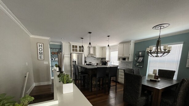 A modern kitchen with white cabinets, a central island, and a dining area with dark wicker chairs.